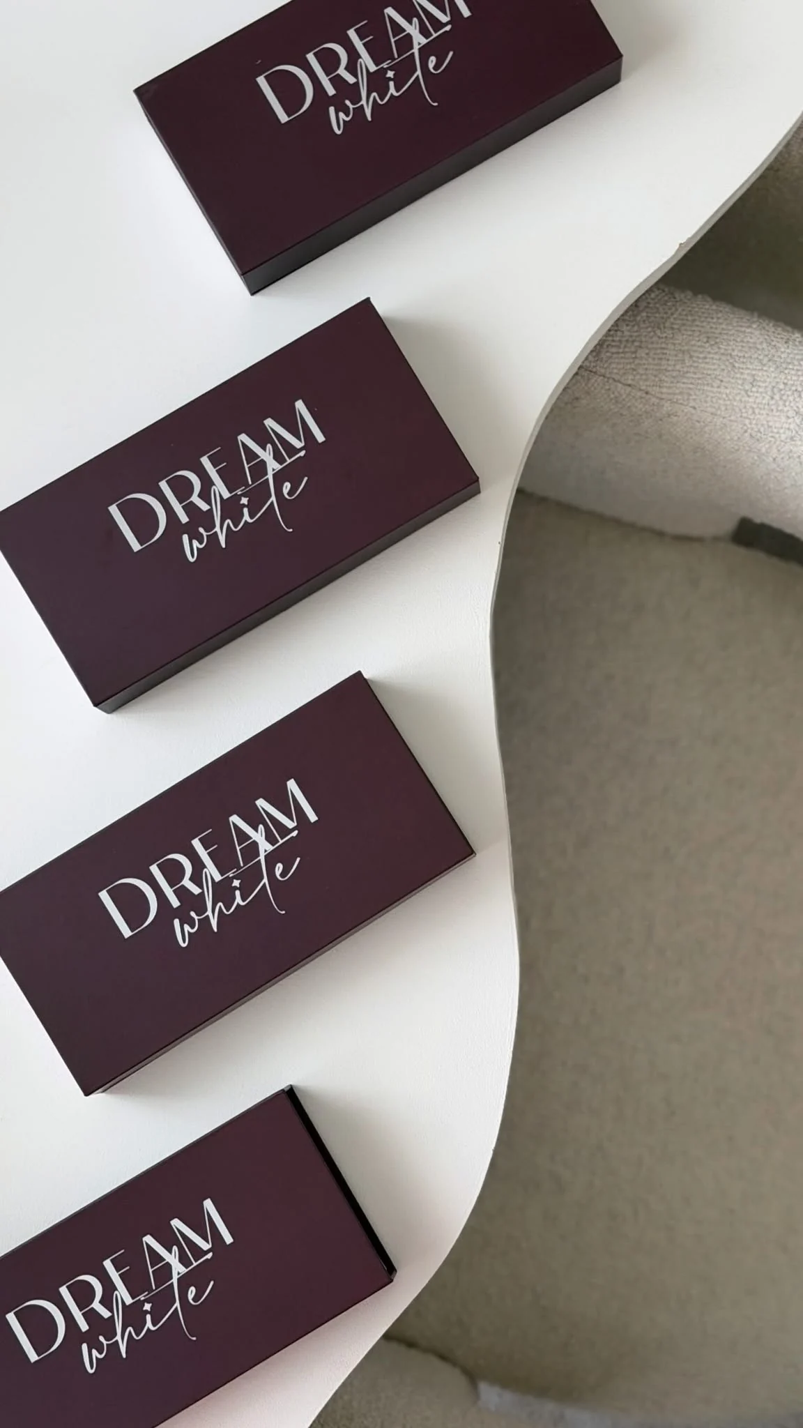 Vier geschlossene Dreamwhite-Boxen auf einem weißen Tisch neben einem hellen Sessel