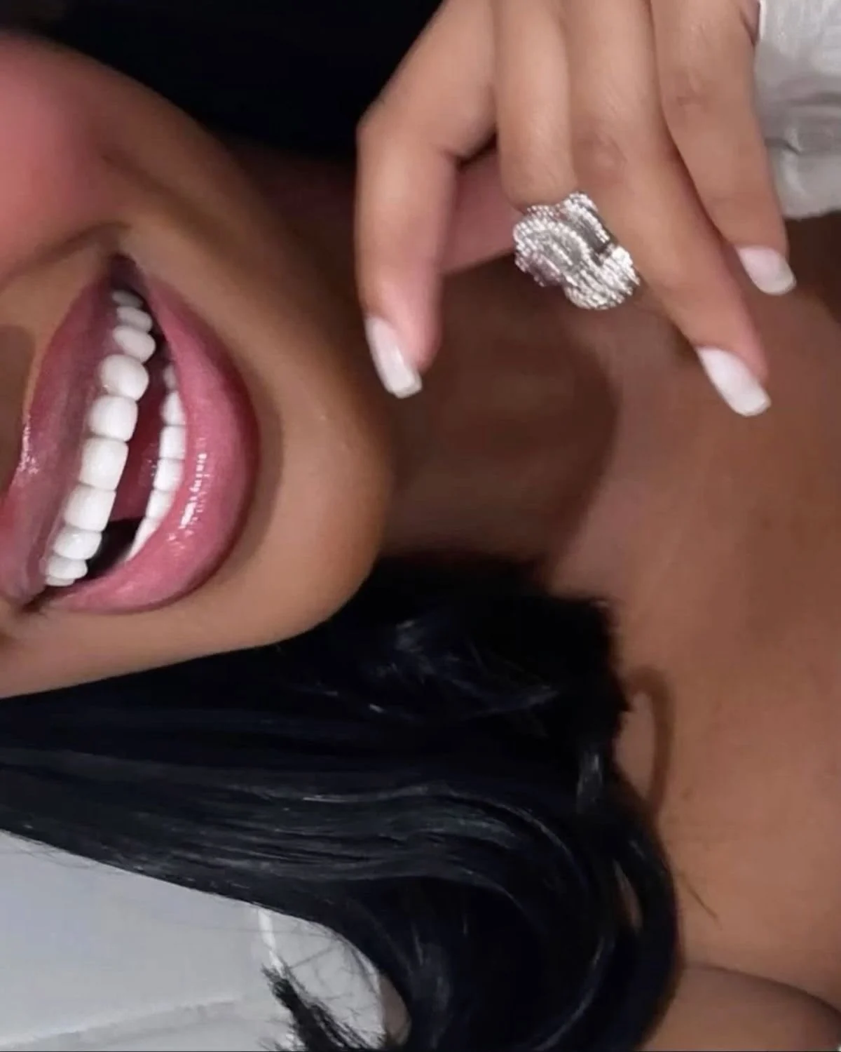 Lachender Mund mit weißen Zähnen, daneben eine Hand mit funkelndem Ring