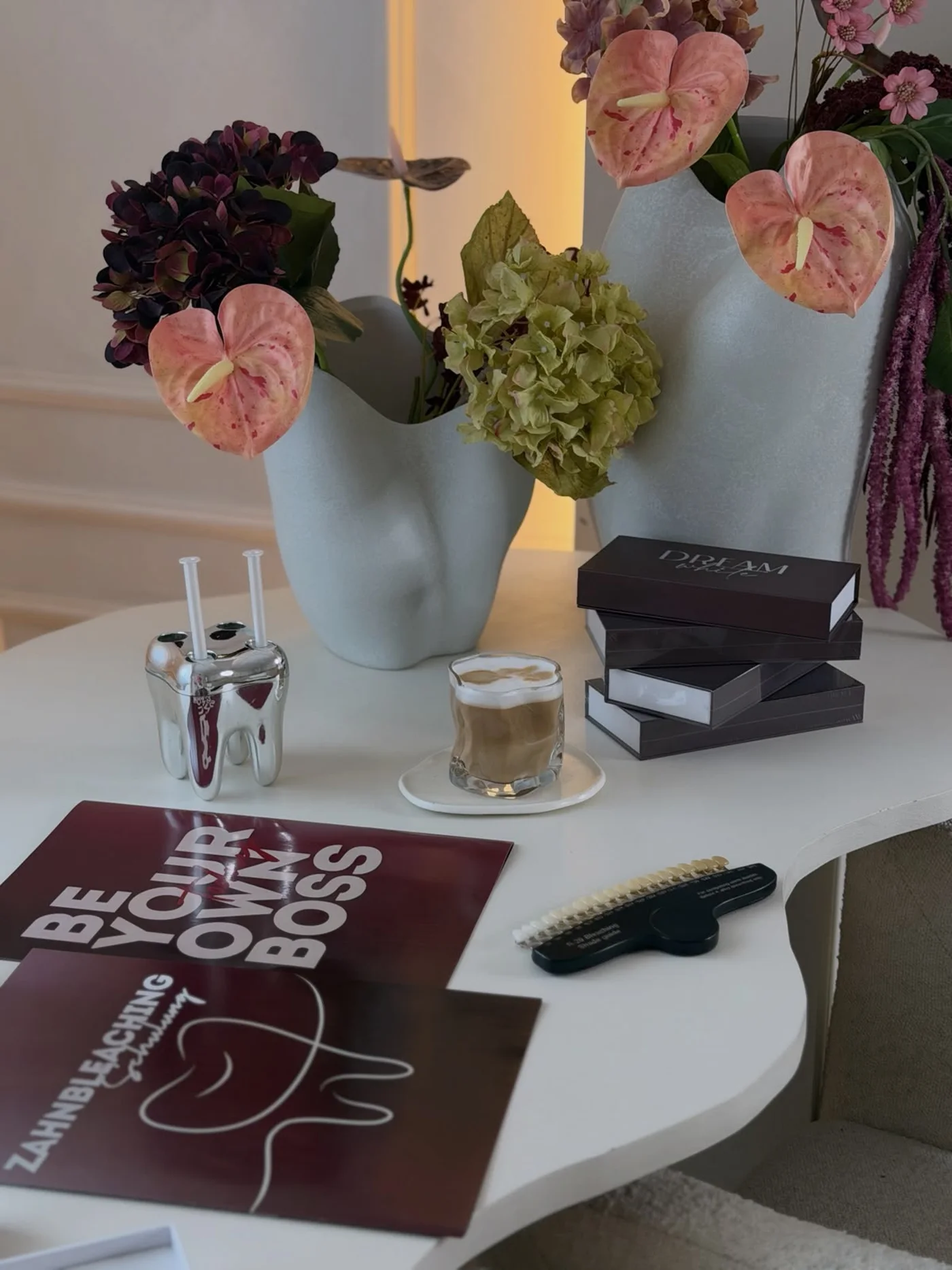 Schulungstisch bei Dreamwhite mit Blumen, gestapelten Dreamwhite-Boxen, Kaffee, Gel-Spritzen und den Unterlagen Be your own boss und Zahnbleaching Schulung